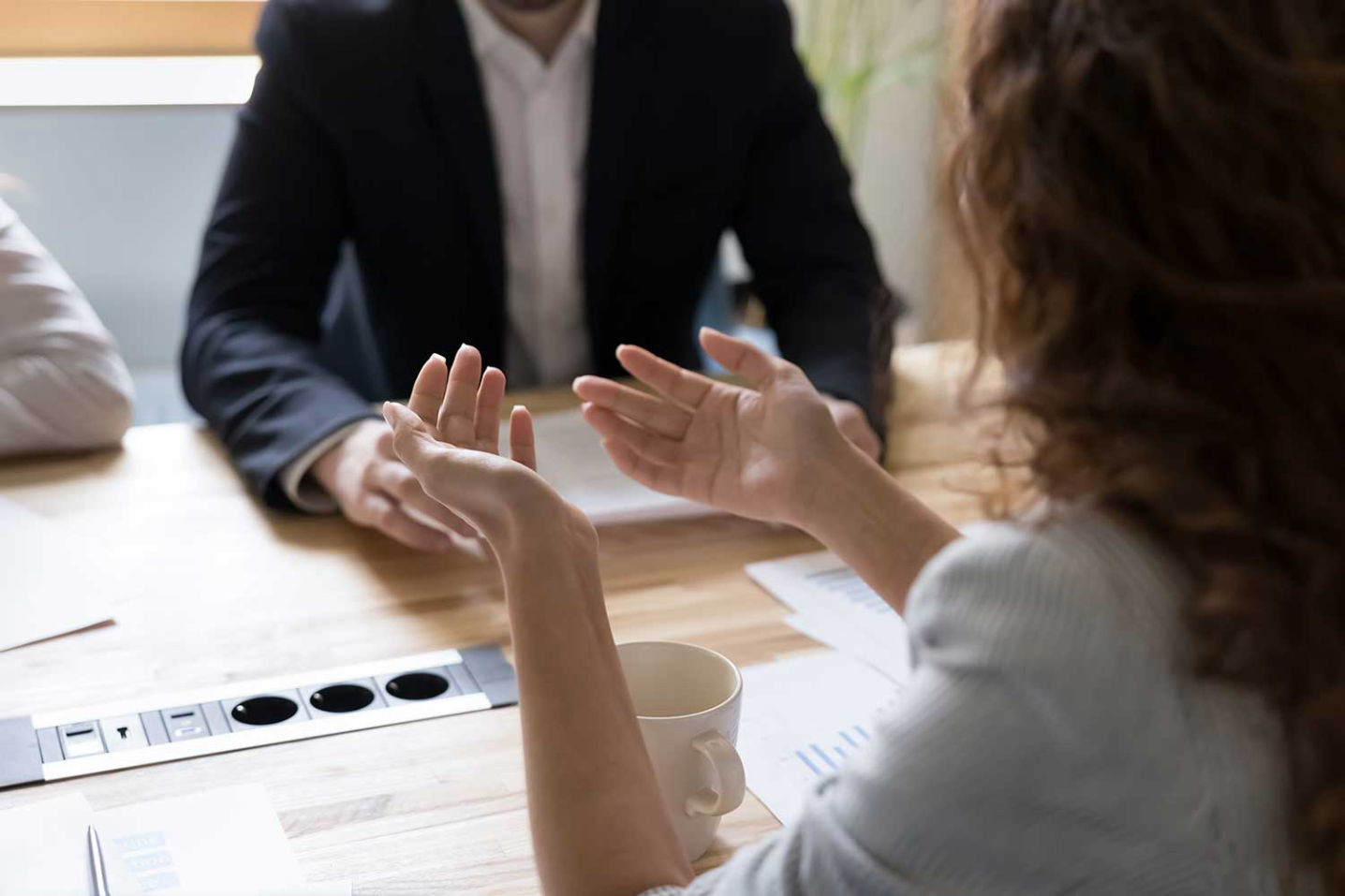 Von hinten sichtbare ur-Businesscoachin diskutiert mit  Fach- und Führungskräften an einem Besprechungstisch